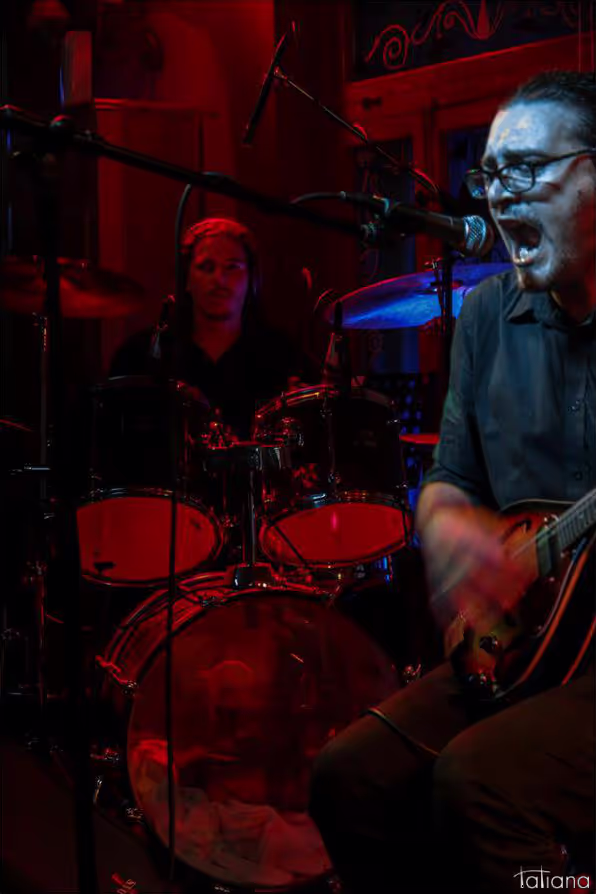 Petros of Come with Reverse singing passionately and playing the mandolin, with Alex (keys) in the background, during a live performance.